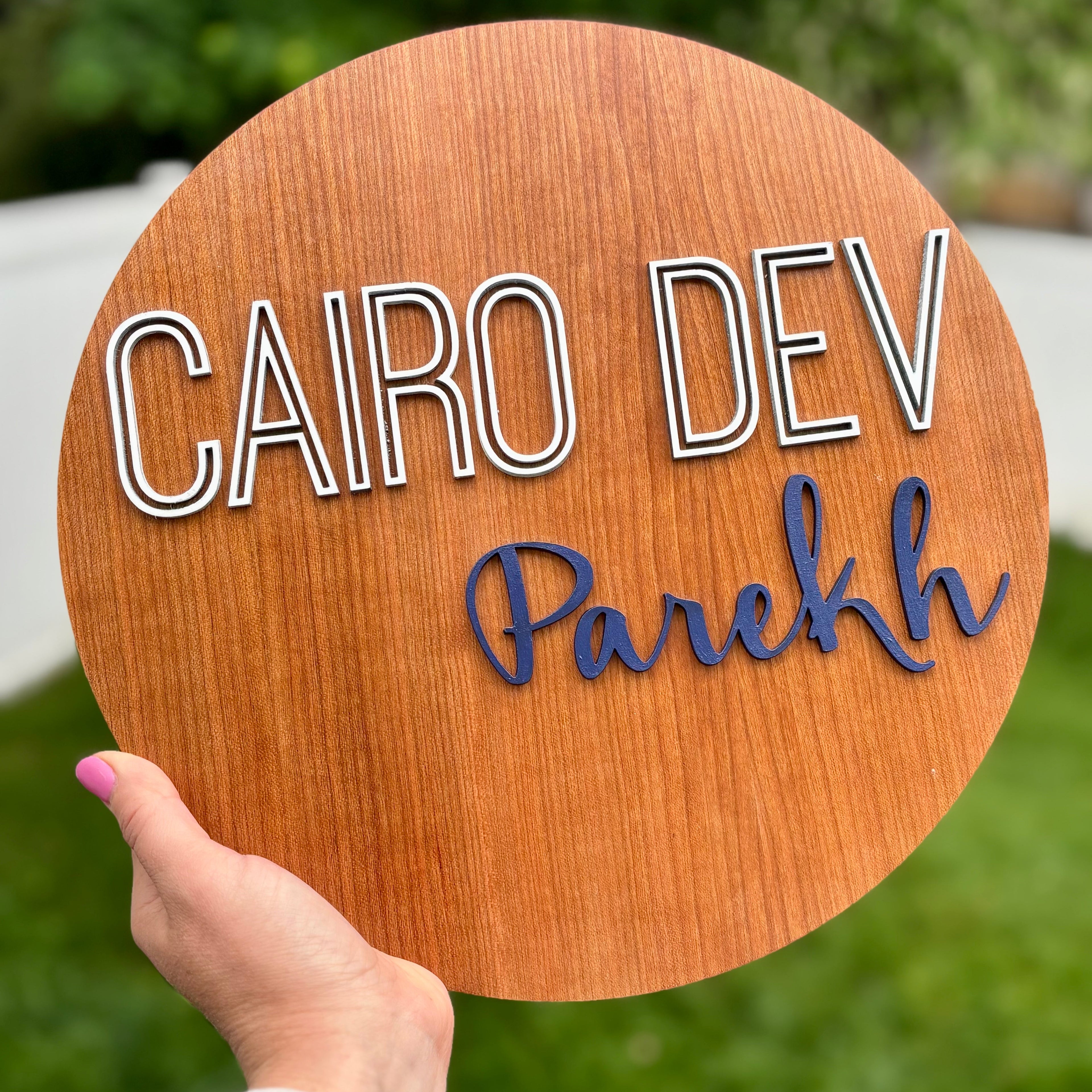 Wooden sign with 'CAIRO DEV Parekh' text held by a hand against a blurred green background